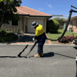 Worker applying sealant to cracks on suburban street asphalt surface