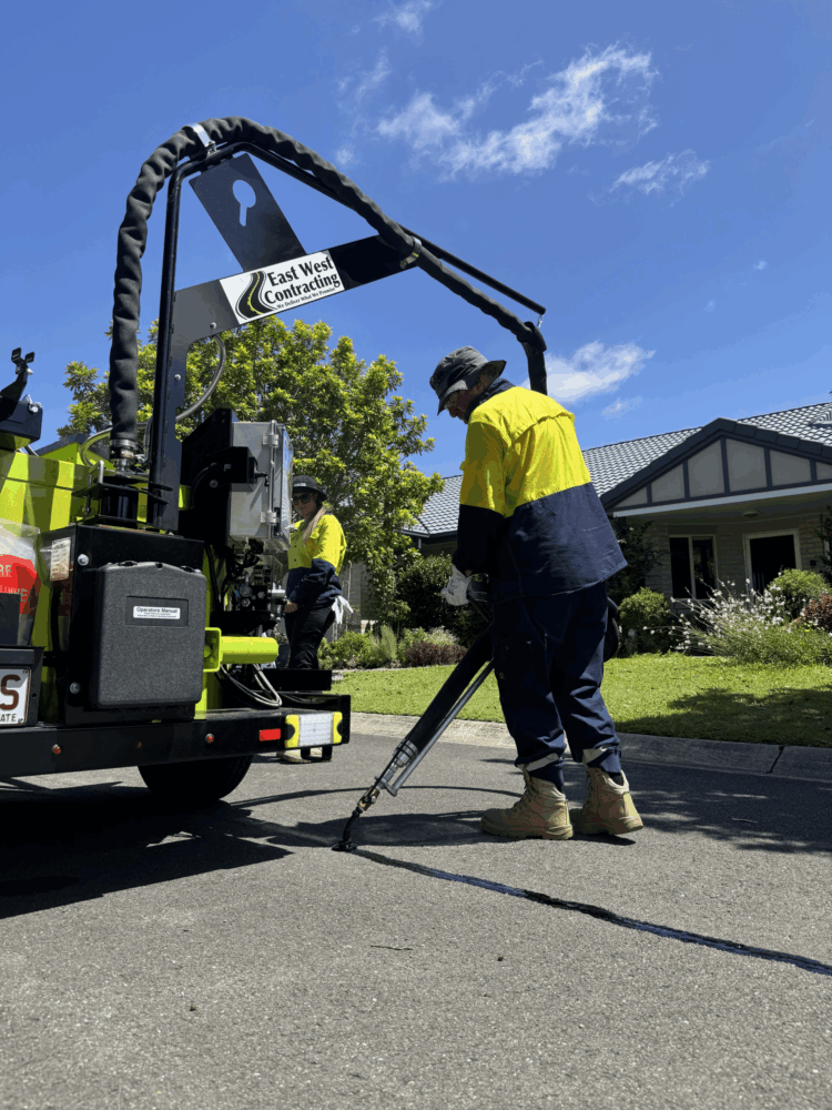 Worker using crack sealing machine on asphalt pavement in residential area