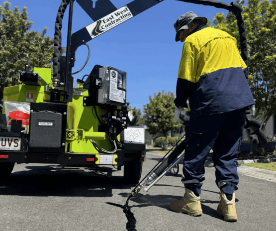 Worker applying hot sealant to asphalt crack using specialized road maintenance equipment